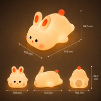 Infographie en français présentant les dimensions d'une veilleuse lapin en silicone allumée en position couchée (143 mm de longueur, 109 mm de largeur et 84,7 mm de hauteur). Au bas, trois visuels illustrent le produit sous différents angles : de face, de profil et de dos, mettant en avant ses détails orange et sa lueur jaune chaleureuse.
