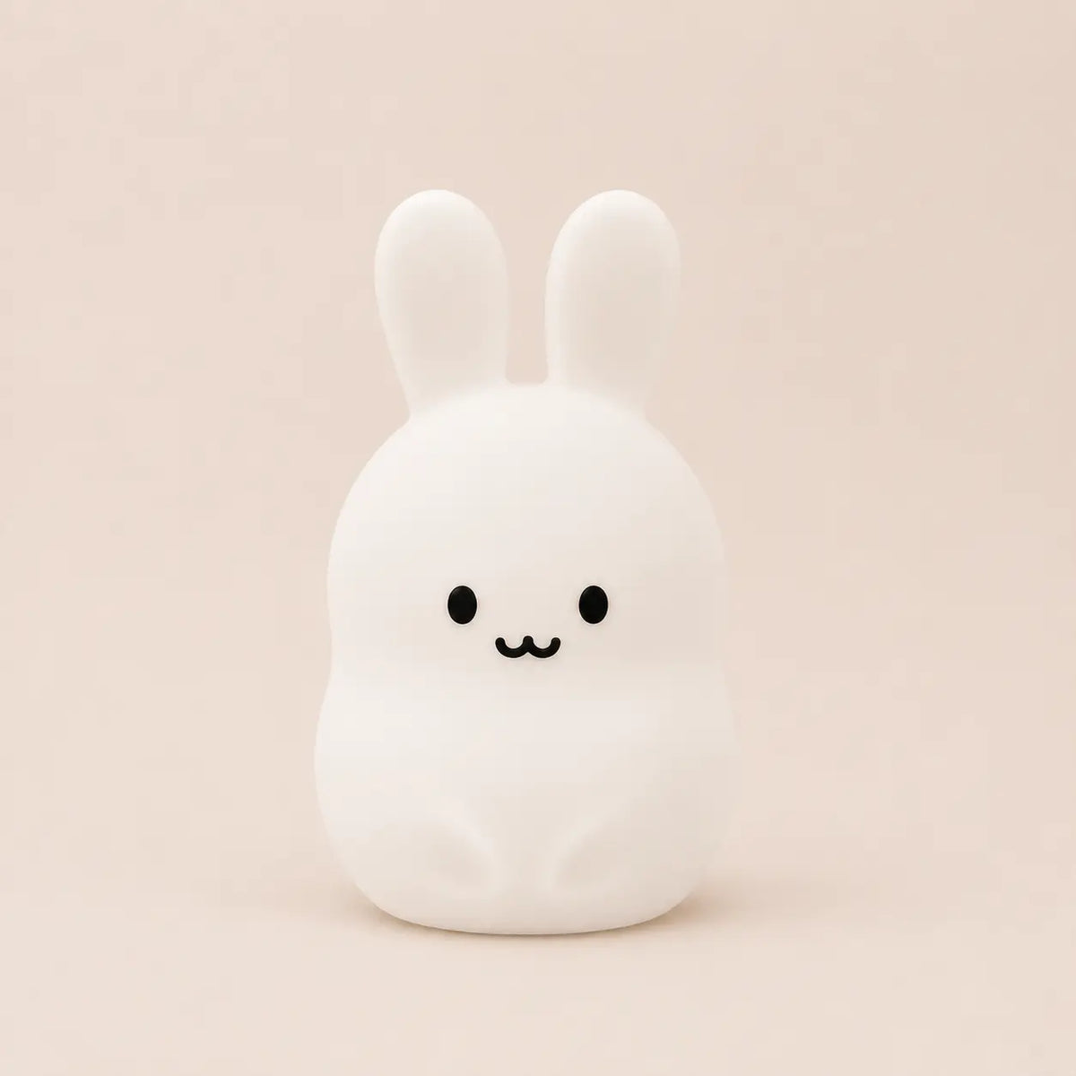 Veilleuse en silicone allumée en forme de petit lapin blanc, sur un fond beige neutre.