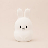 Veilleuse en silicone allumée en forme de petit lapin blanc, sur un fond beige neutre.