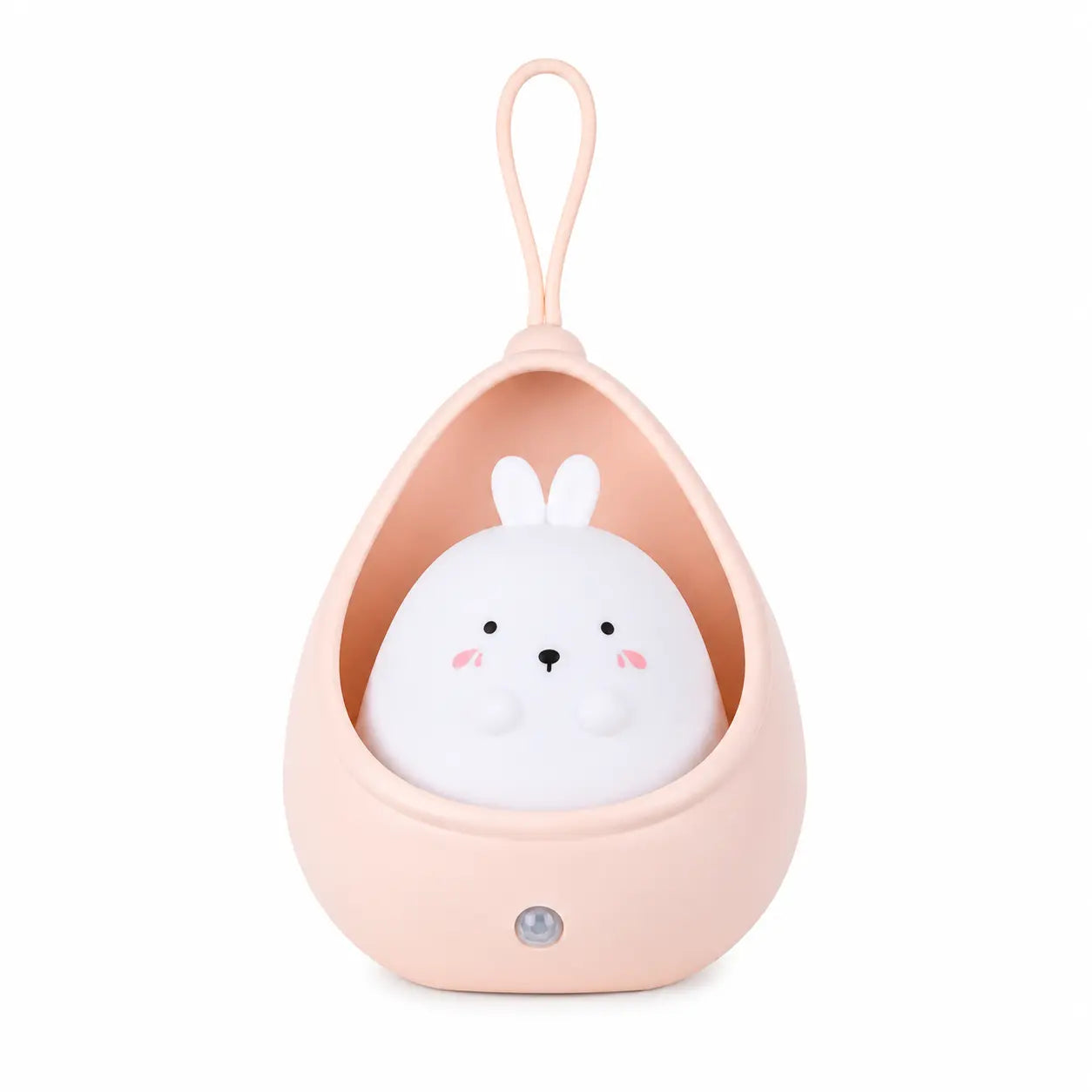 Veilleuse pour bébé représentant un petit lapin blanc aux joues roses logé à l'intérieur d'un cocon protecteur en forme de goutte couleur rose poudré. Le modèle comprend une anse en silicone sur le dessus dédiée à la suspension et un détecteur de mouvement circulaire intégré sur la partie inférieure de la base, présentée de face sur fond blanc.