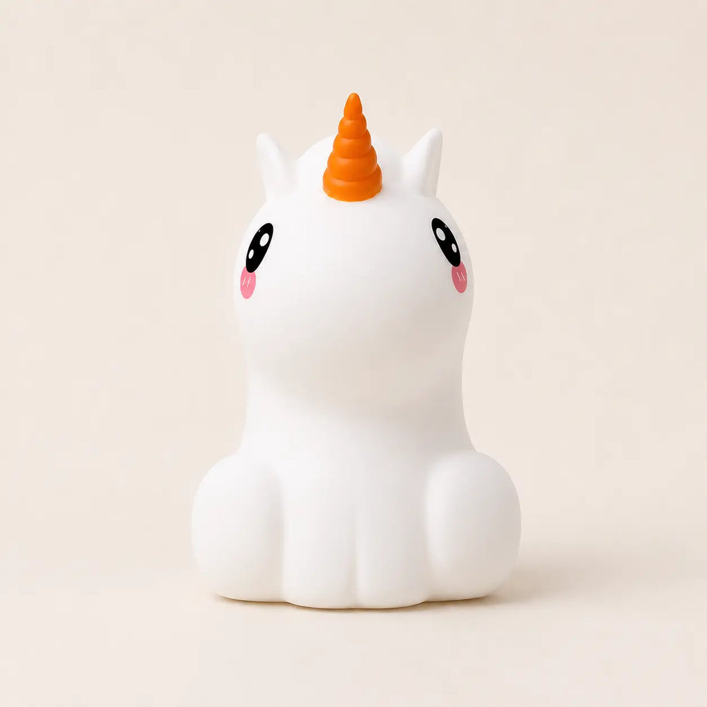 Veilleuse en silicone en forme de petite licorne blanche avec une corne orange, sur un fond beige neutre.