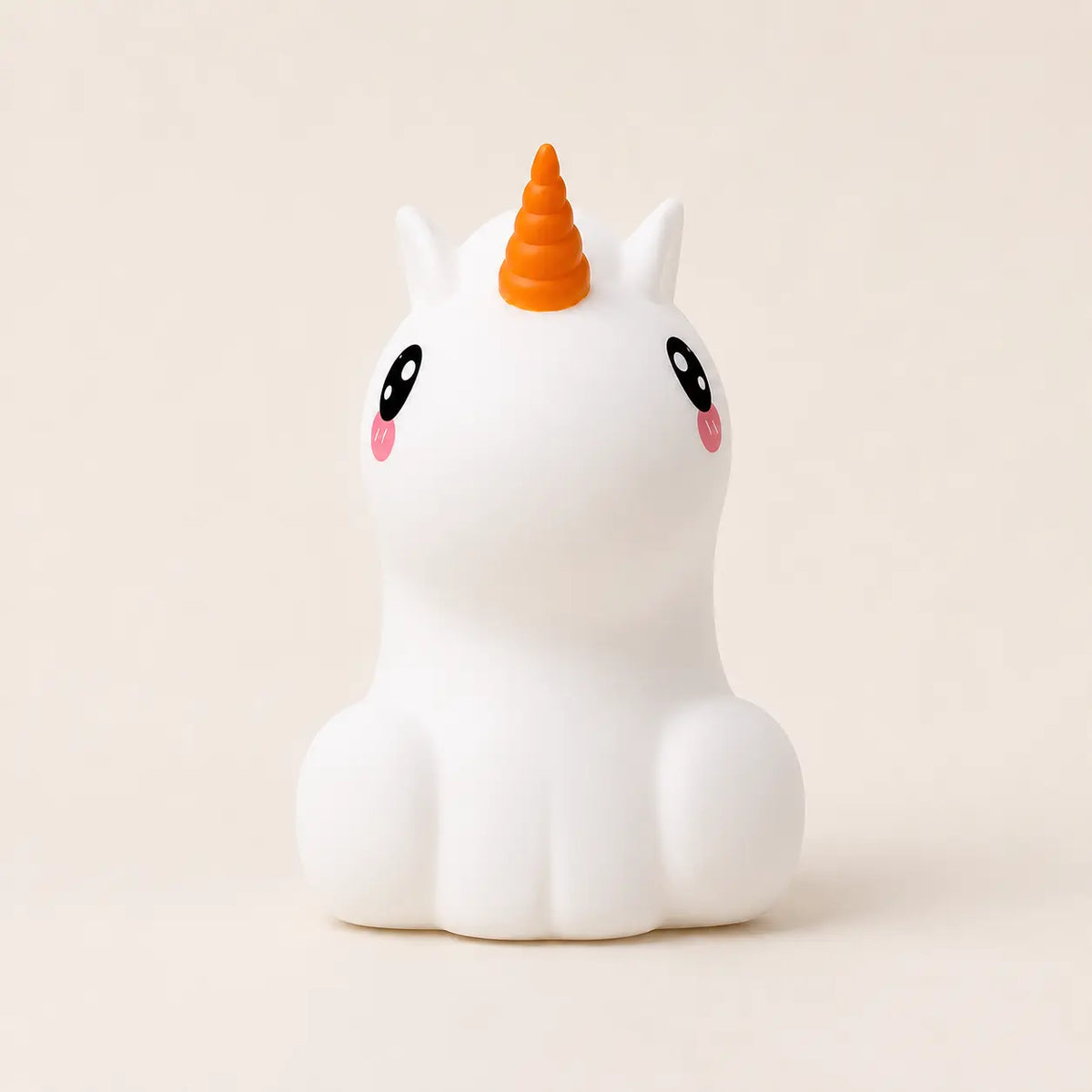 Veilleuse en silicone en forme de petite licorne blanche avec une corne orange, sur un fond beige neutre.