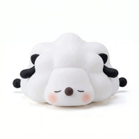 Veilleuse en silicone en forme de petit mouton blanc et noir couché aux yeux fermés, sur un fond blanc.