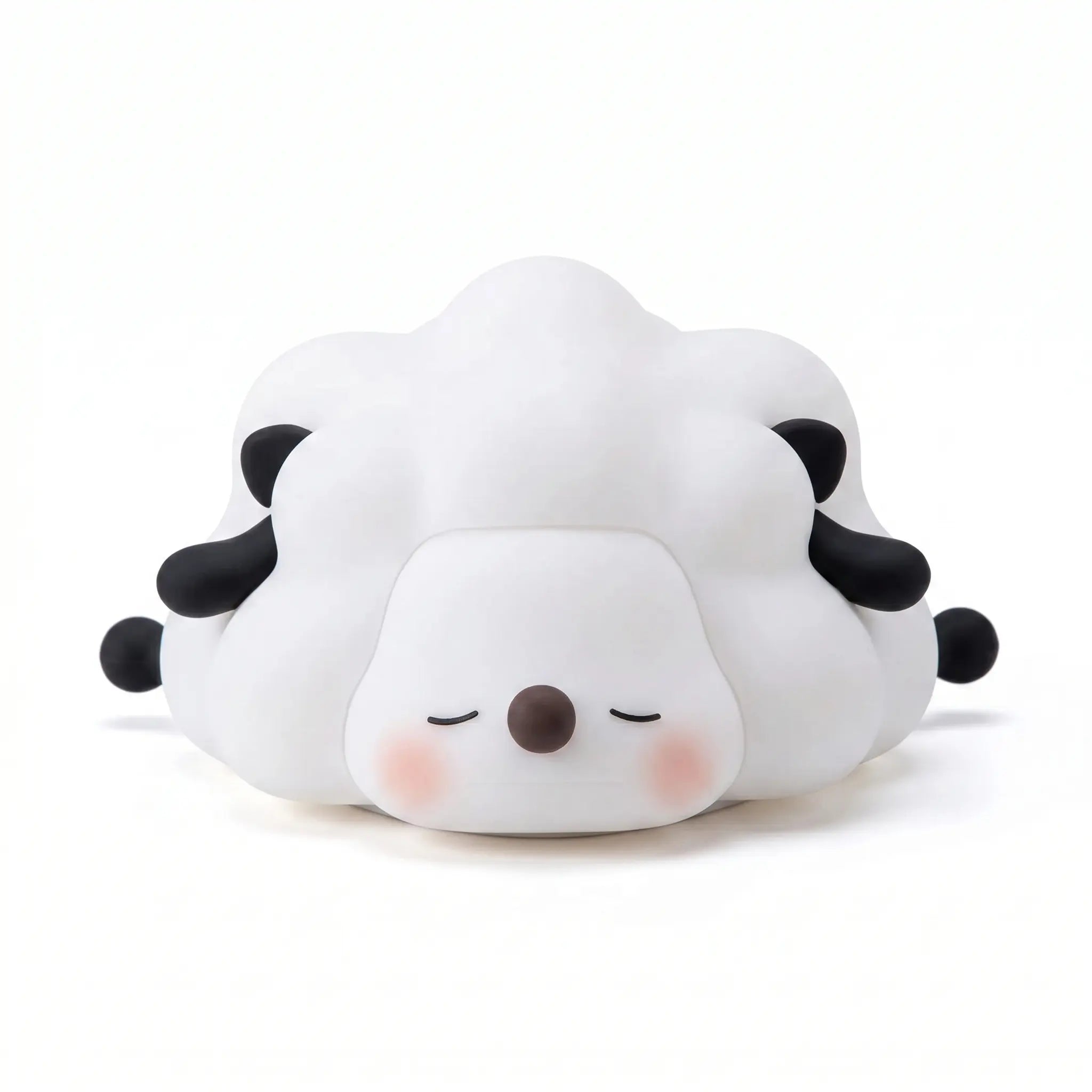Veilleuse en silicone en forme de petit mouton blanc et noir couché aux yeux fermés, sur un fond blanc.