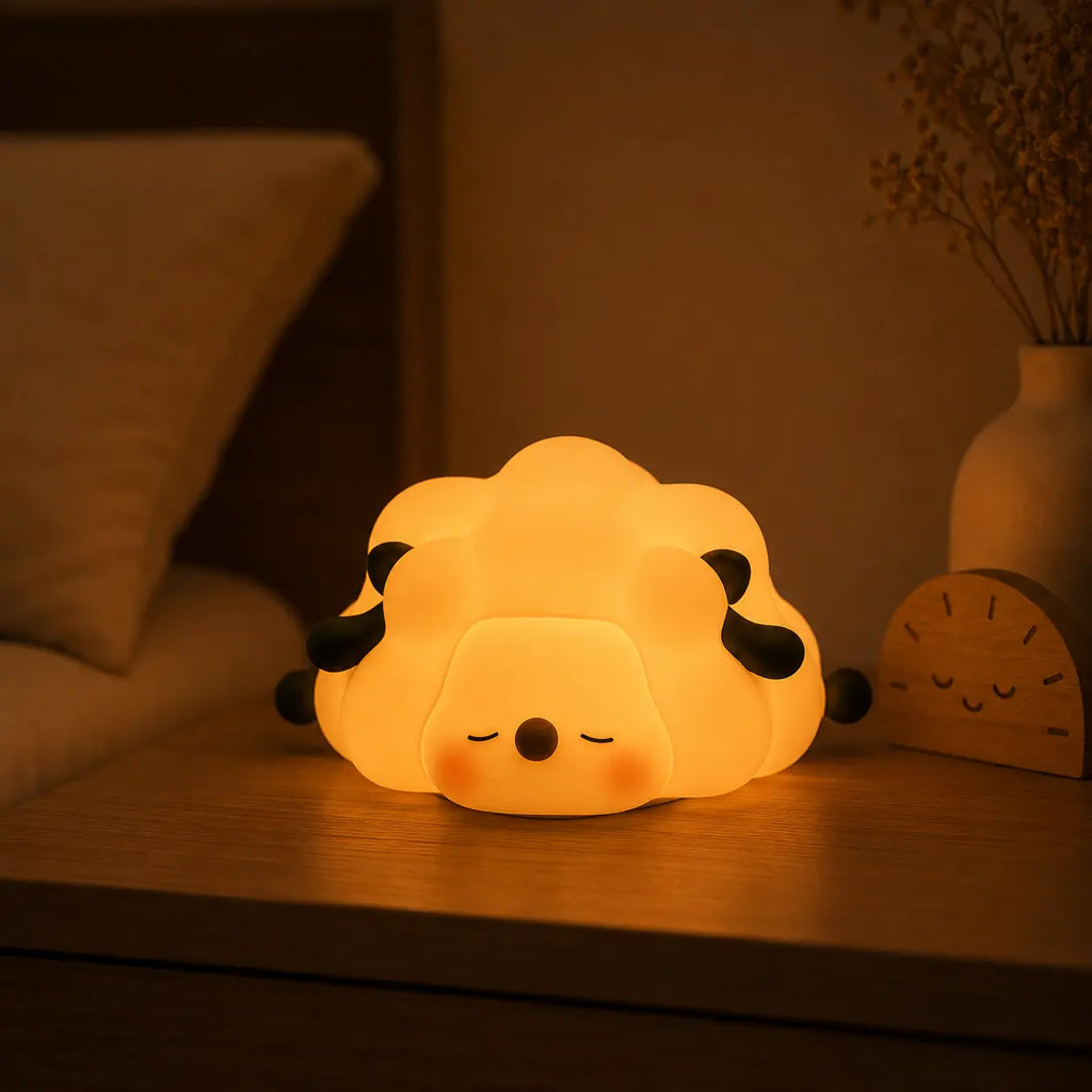 Veilleuse en forme de petit mouton couché allumée posée sur une table de chevet dans une ambiance chaleureuse.