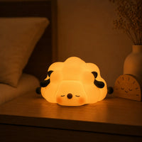 Veilleuse en forme de petit mouton couché allumée posée sur une table de chevet dans une ambiance chaleureuse.
