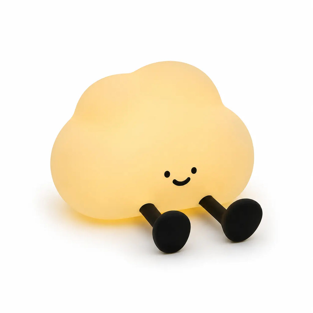Veilleuse en silicone en forme de petit nuage jaune allumée, dotée de deux petites jambes noires allongées vers l'avant. Elle affiche un visage au sourire minimaliste et mignon, présentée de face sur un fond blanc épuré.
