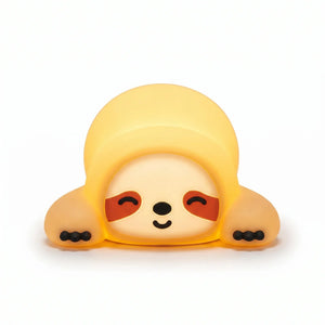 Veilleuse en silicone en forme de petit paresseux allongé tout mignon. Elle affiche un visage serein avec des yeux clos souriants, des taches marron caractéristiques et de petites griffes noires, diffusant une douce lueur jaune tamisée sur un fond blanc épuré.