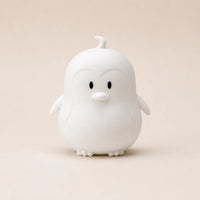 Veilleuse en silicone en forme de petit pingouin blanc, sur un fond beige neutre.