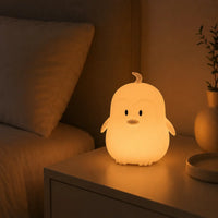 Veilleuse en forme de petit pingouin allumée posée sur une table de chevet dans l'obscurité.