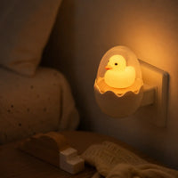 Veilleuse prise murale canard dans son œuf allumée diffusant une lumière douce dans une chambre d'enfant