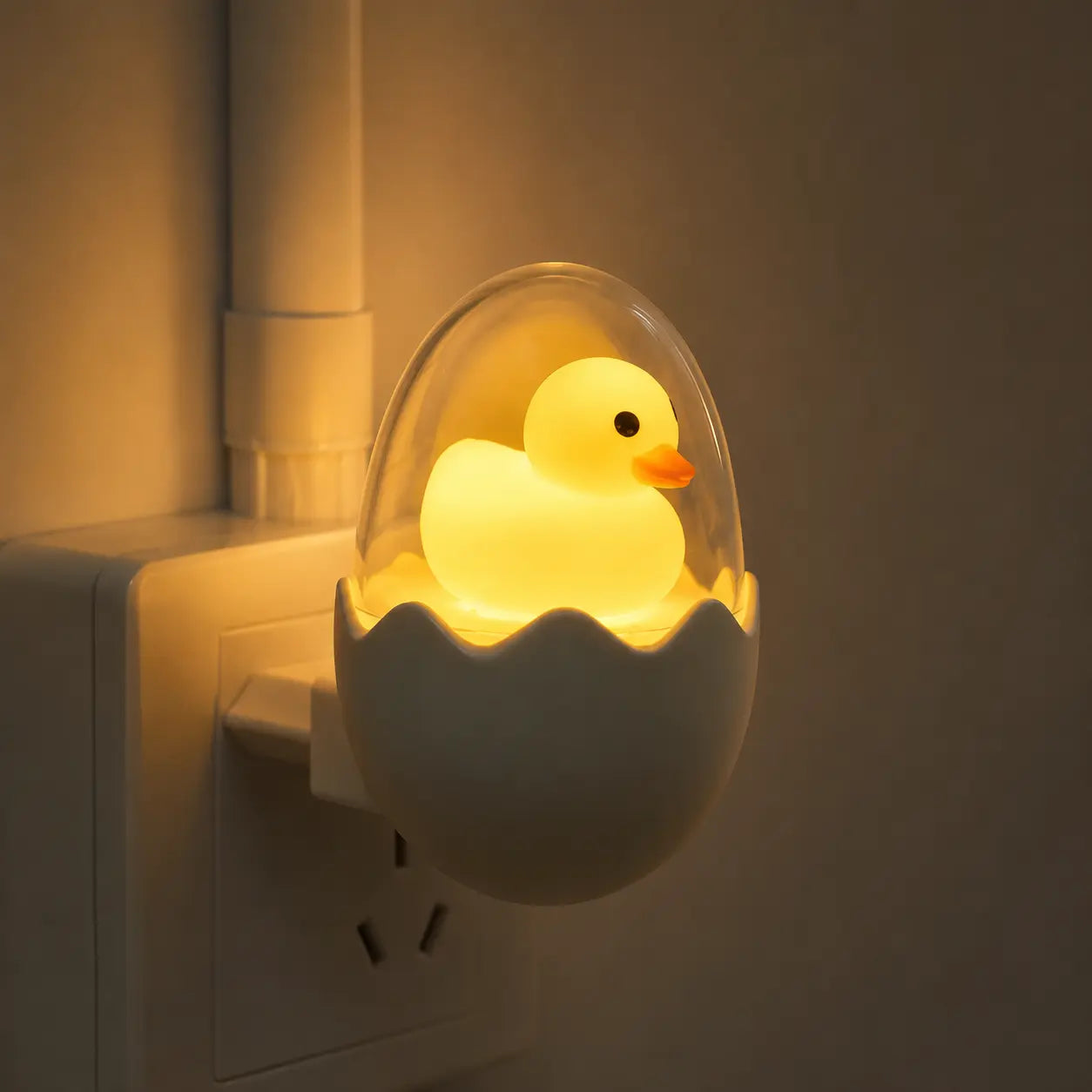 Gros plan sur la veilleuse prise canard illuminée dans sa coquille d'œuf branchée sur une prise murale