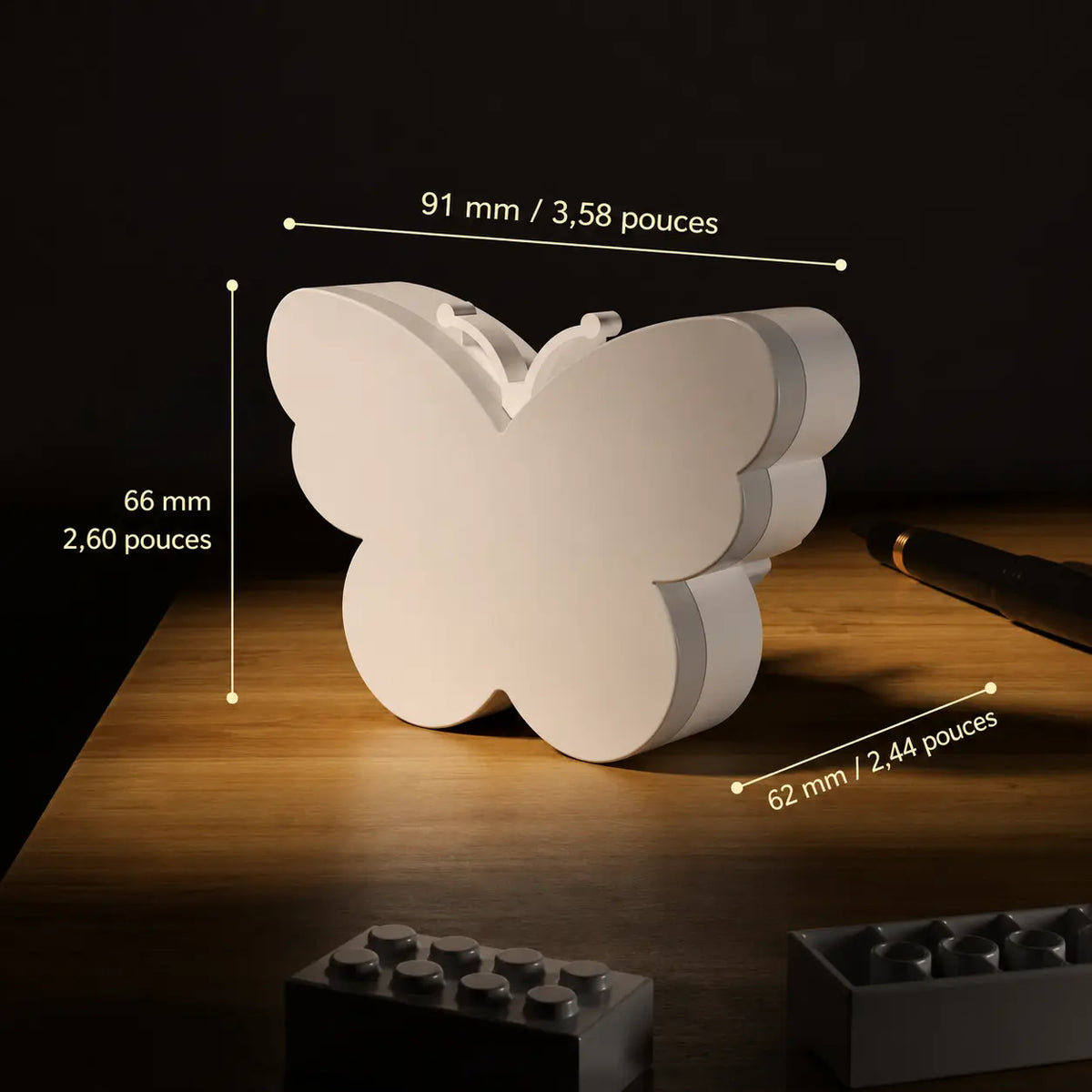 Infographie indiquant les dimensions de la veilleuse prise en forme de papillon posée sur un meuble en bois.