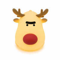 Veilleuse en silicone en forme de petit renne de Noël allumée, avec un gros nez rouge, des bois bruns et une expression amusante aux sourcils froncés, diffusant une lueur chaleureuse, présentée de face sur fond blanc.