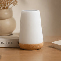 Veilleuse style scandinave avec interrupteur et port de charge apparents sur sa base en bois, installée à côté d'un livre de décoration.