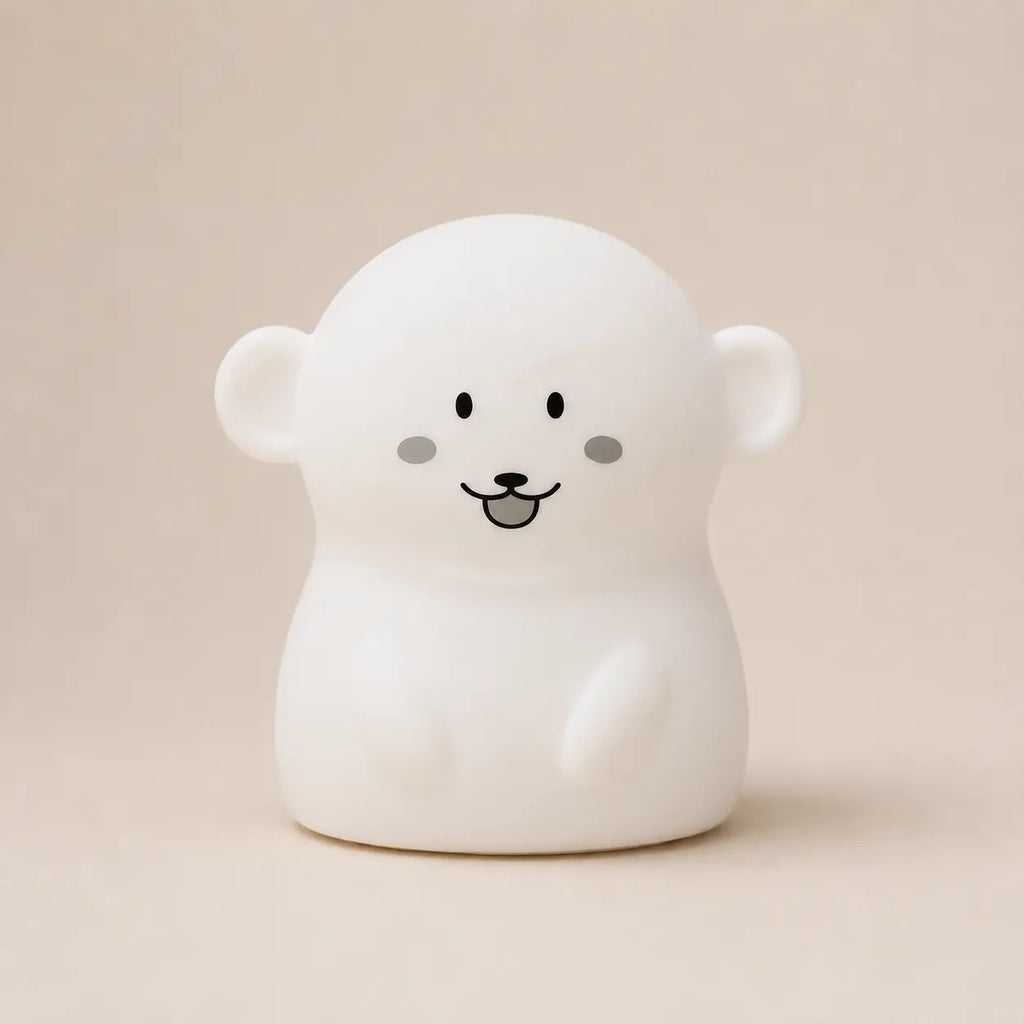 Veilleuse en silicone en forme de petit singe blanc, sur un fond beige neutre.