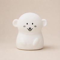 Veilleuse en silicone en forme de petit singe blanc, sur un fond beige neutre.