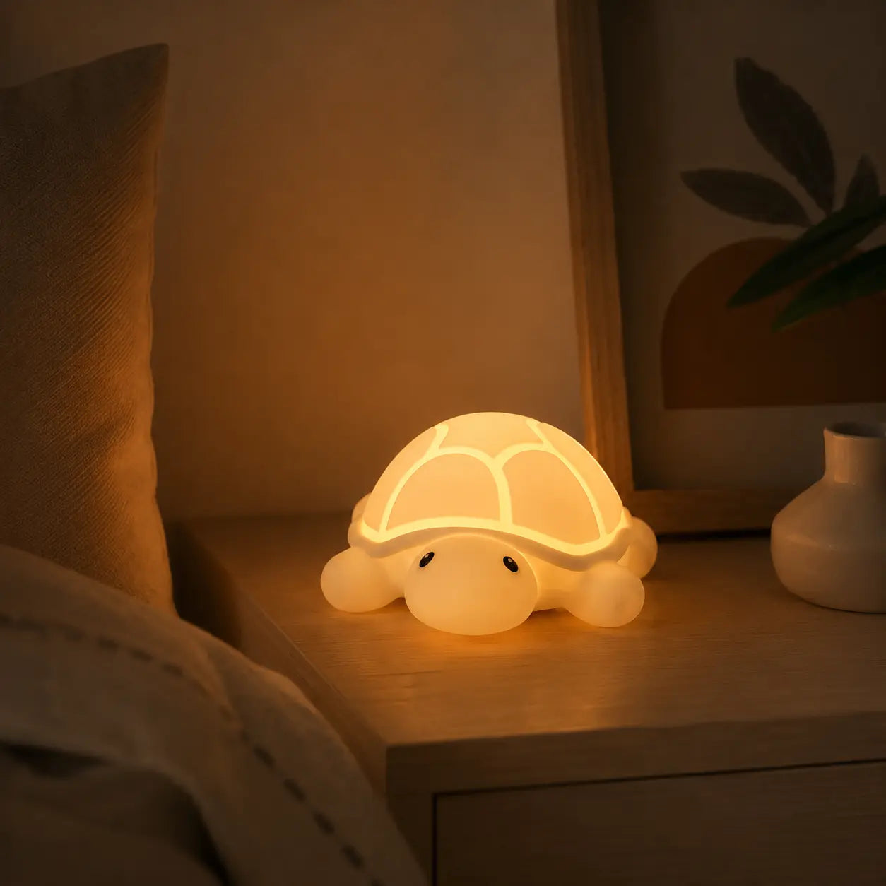 Veilleuse bébé en silicone souple en forme de petite tortue allumée, diffusant une douce lueur chaude sur une table de chevet en bois dans une chambre d'enfant à l'ambiance tamisée et sereine.