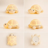 Planche produit d'une veilleuse tortue en silicone souple allumée sous six angles différents : de face, de trois-quarts, de profil, de trois-quarts arrière, vue du dessus mettant en valeur les motifs du dos, et vue du dessous montrant le bouton d'alimentation et le port de charge.